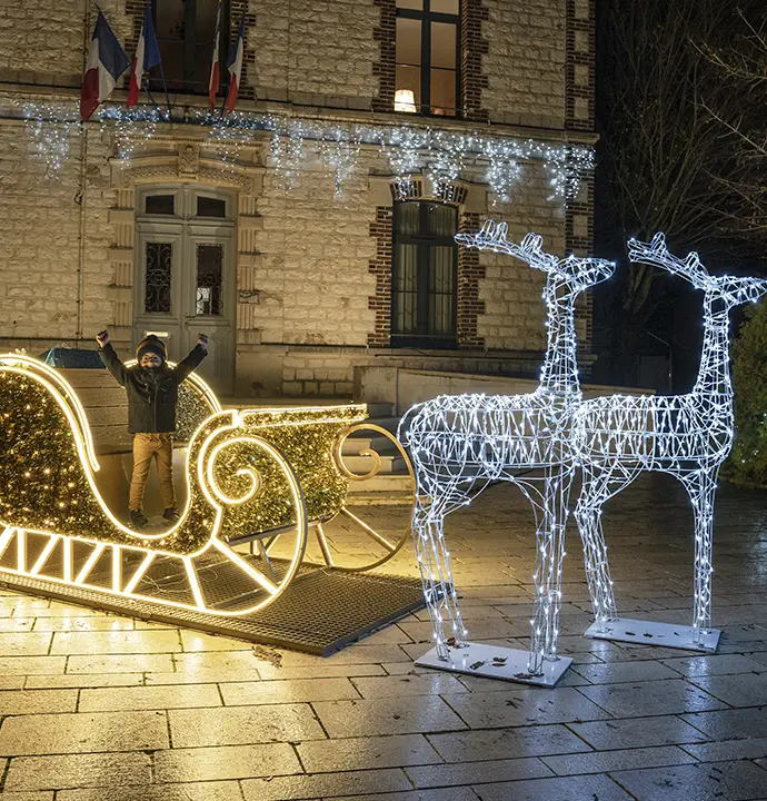 Place de village décoré pour noël avec un traineau et des rennes lumineux